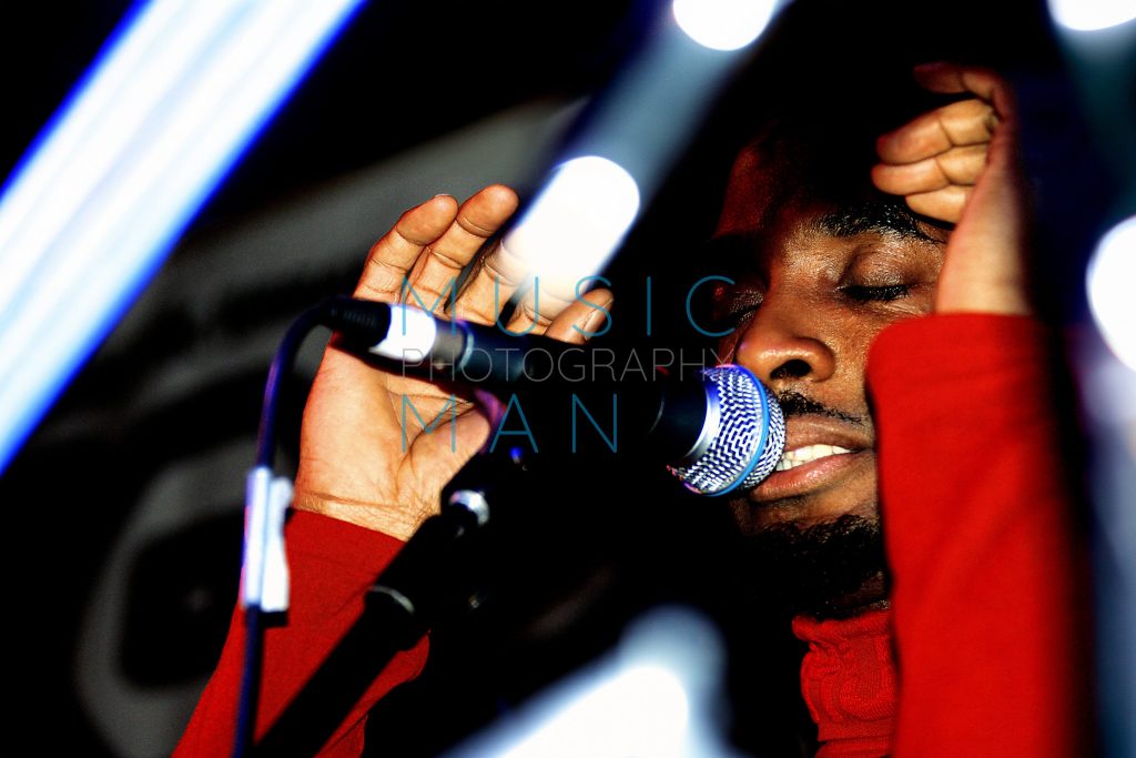 Musician Amp Fiddler performing live on stage framed by abstract foreground light bokeh at the Jazz Café in London, photography by Music Man Studio.