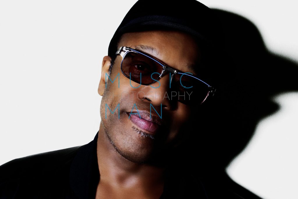 Soul music icon Bobby Womack posing in a black cap and designer sunglasses with iridescent purple lens reflections during a high-contrast London studio portrait session, photography by Music Man Studio.