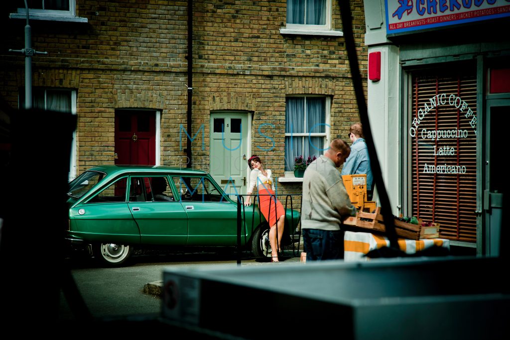 Singer Cheryl Cole on the 1960s retro street set of her Under the Sun music video at Wimbledon Studios, leaning against a classic mint-green vintage Citroën Ami Super car, behind-the-scenes photography by Music Man Studio.