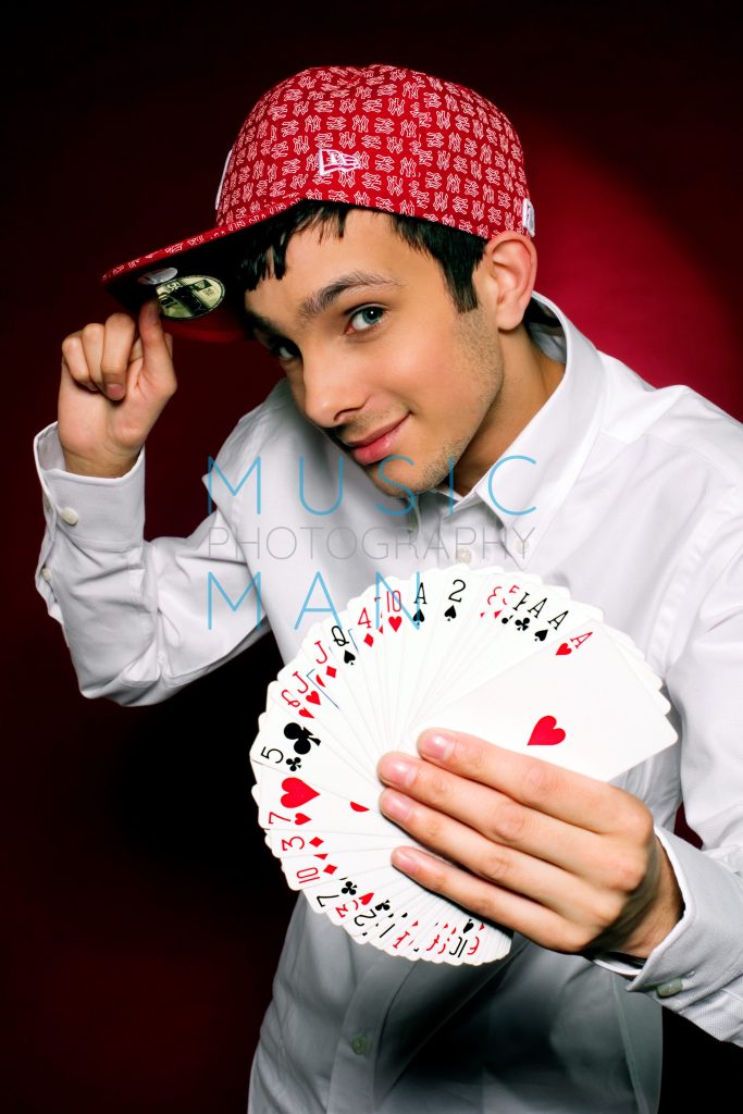 Magician Dynamo fanning a deck of playing cards and tipping a red cap during a Clerkenwell studio portrait session for the Body and Soul charity campaign featured across the London Underground network, photography by Music Man Studio