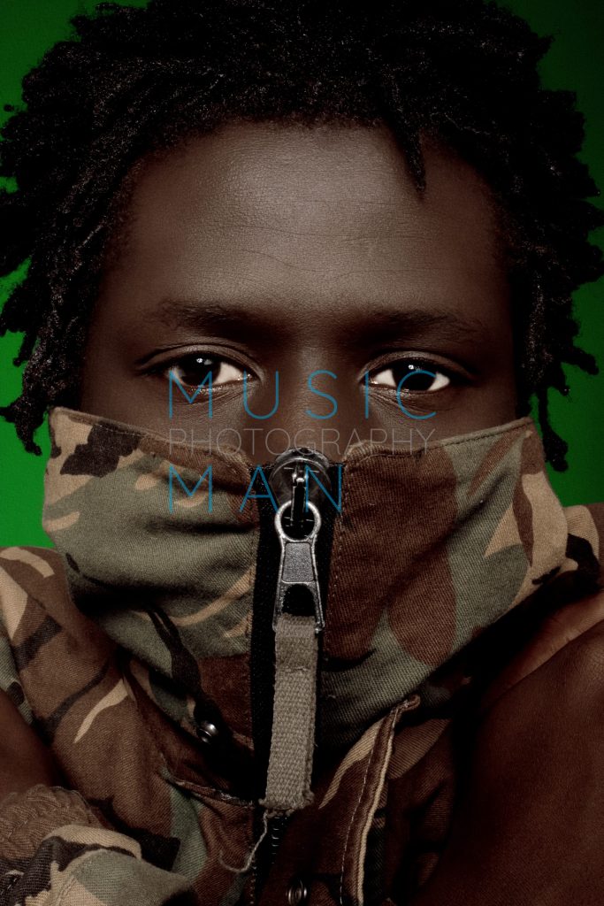South Sudanese hip-hop artist Emmanuel Jal wearing a zipped military camouflage jacket during an exclusive Clerkenwell studio portrait session, photography by Music Man Studio.