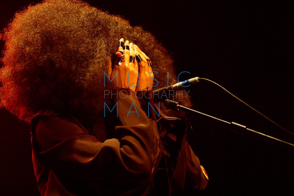 Singer Erykah Badu captured in an intimate profile moment with her face covered by ring-clad hands and framed by a large Afro silhouette live at Brixton Academy, photography by Music Man Studio.