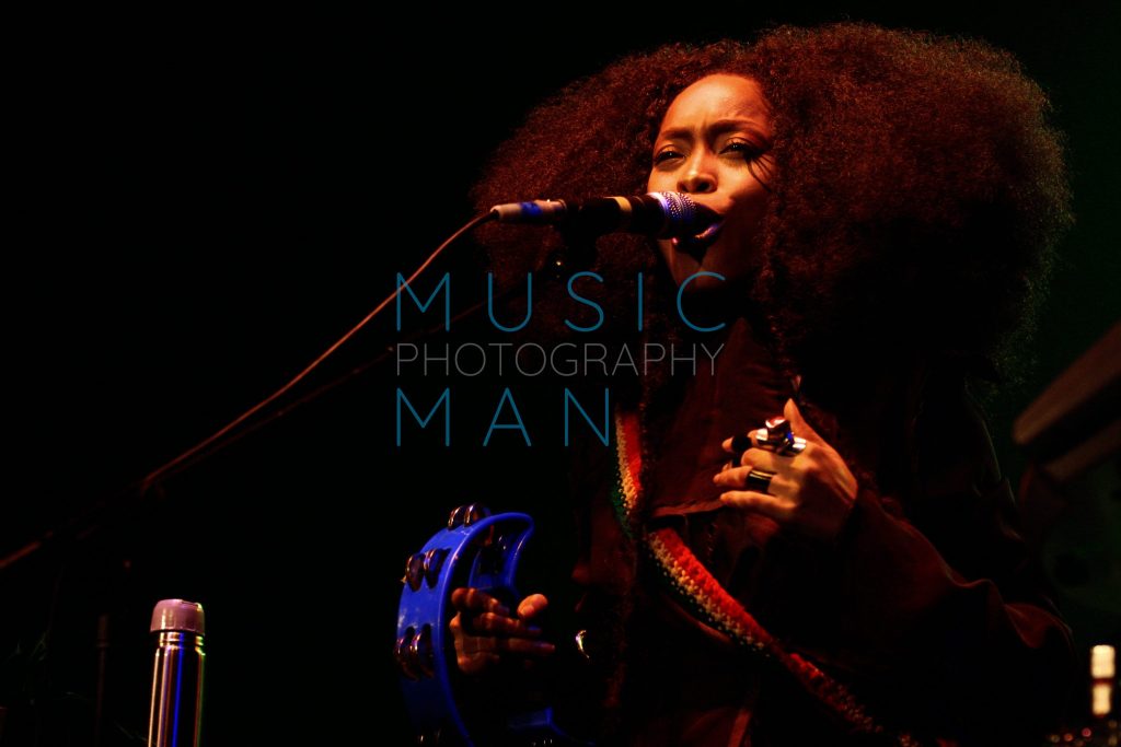 Singer Erykah Badu performing live on stage with a blue tambourine at the Brixton Academy in London, archival concert photography by Music Man Studio.