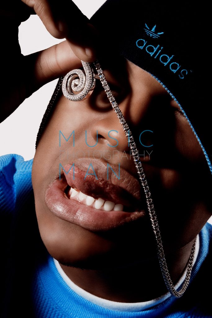 R&B artist Ne-Yo sticking his tongue out while holding up a flashing diamond encrusted chain and wearing a blue Adidas beanie, hotel cupboard studio photography by Music Man Studio.