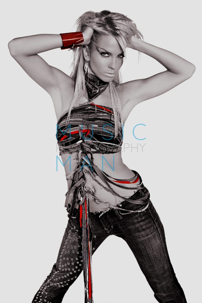 Singer Sarah Harding of Girls Aloud posing on the post-apocalyptic set of the Wake Me Up music video at Pinewood Studios, wearing a cutout distressed denim top, behind-the-scenes selective color photography by Music Man Studio.