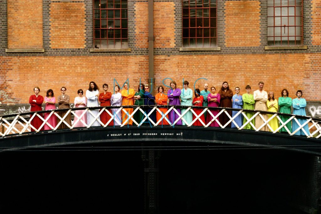 The Polyphonic Spree band members lined up across the iron footbridge at Camden Lock in London wearing their iconic rainbow robes for a featured assignment in The Independent newspaper and supplement magazine, wide angle photography by Music Man Studio.