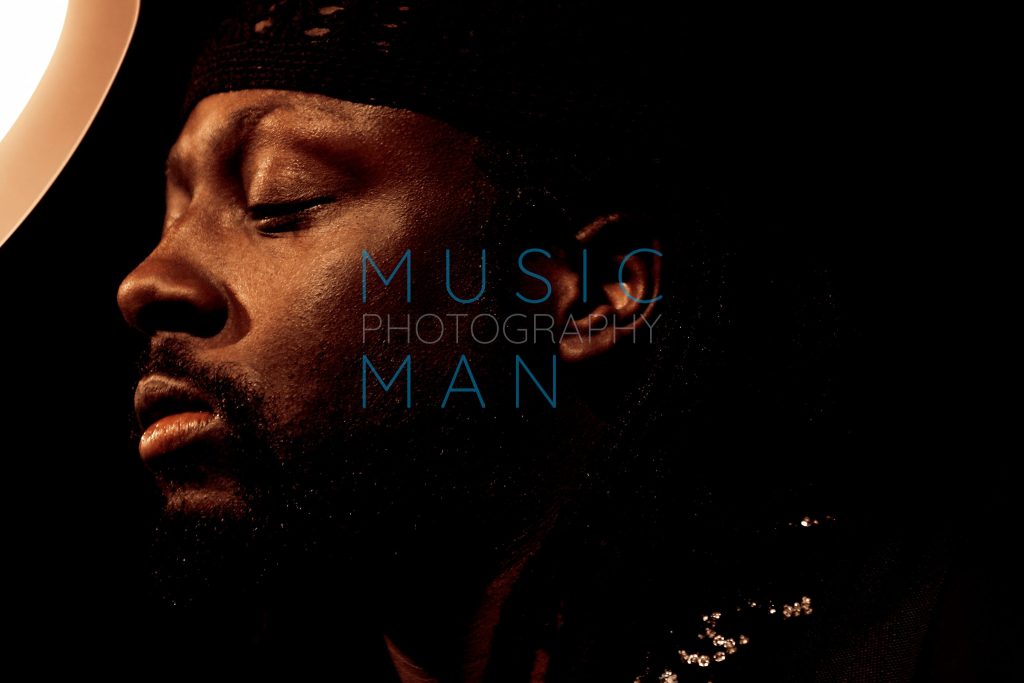 Fugees musician Wyclef Jean captured in profile looking downward in concentration on stage during a private album showcase in London, photography by Music Man Studio.
