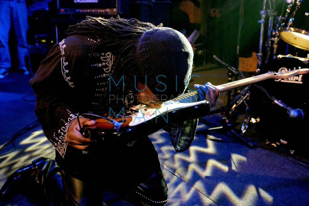 Fugees member Wyclef Jean on his knees playing his electric guitar with his teeth on stage during an exclusive London album showcase, photography by Music Man Studio.